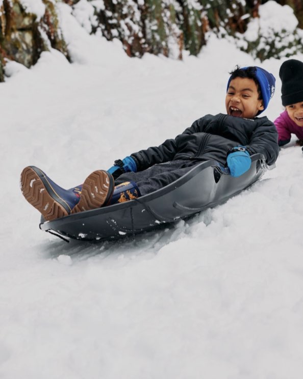 Image features the kids Classic II Dino boot on a young boy sledding.