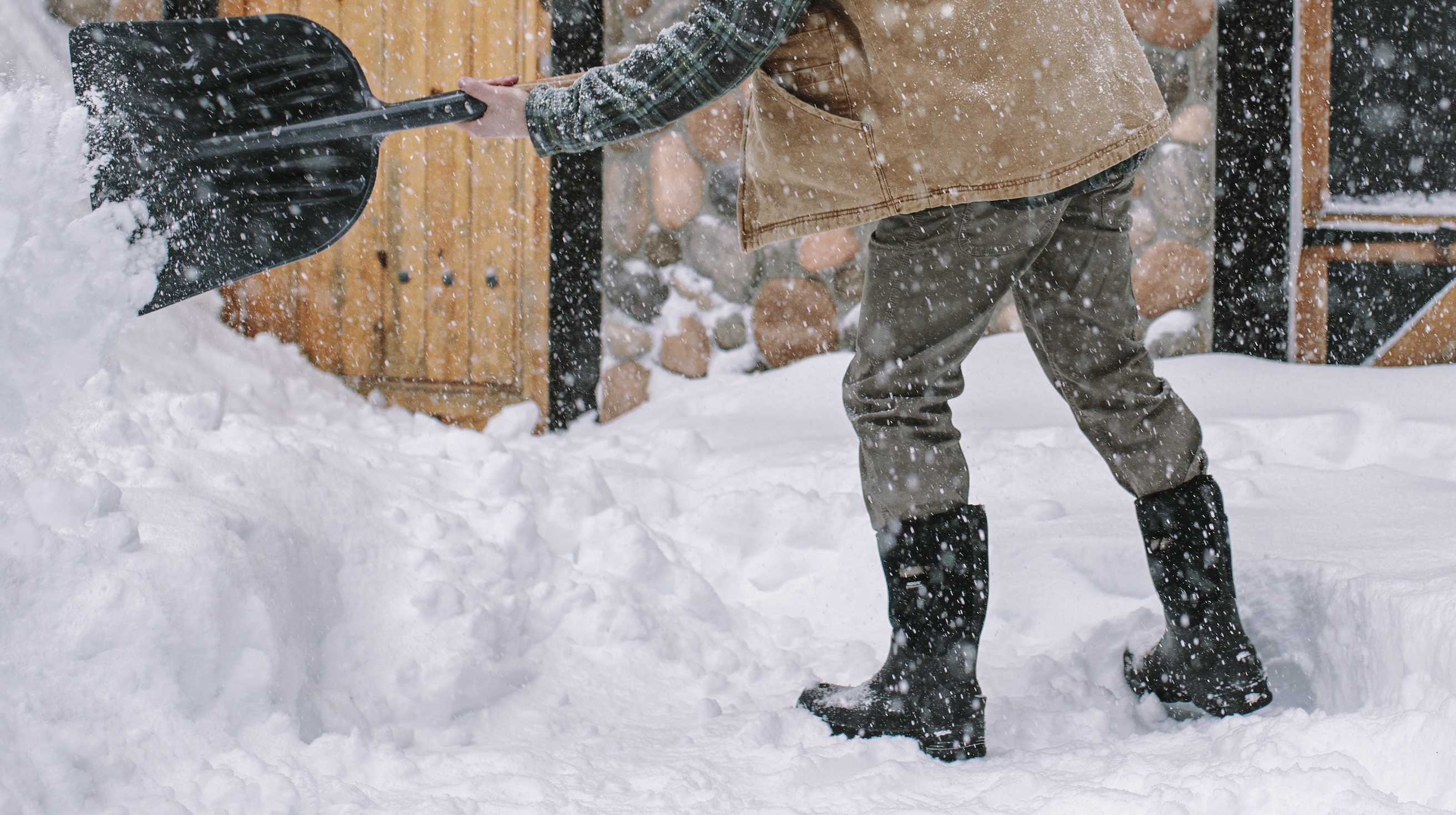 The image shown is a man shoveling snow outside of their cabin.  Shop our top Men’s winter boots. 