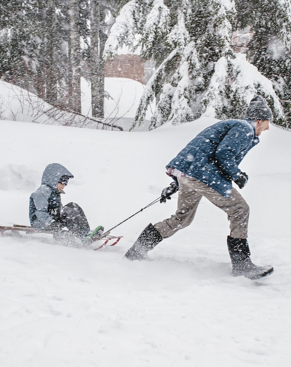 The image shown is a man running & pulling a child on a sled through a snowy winter landscape.