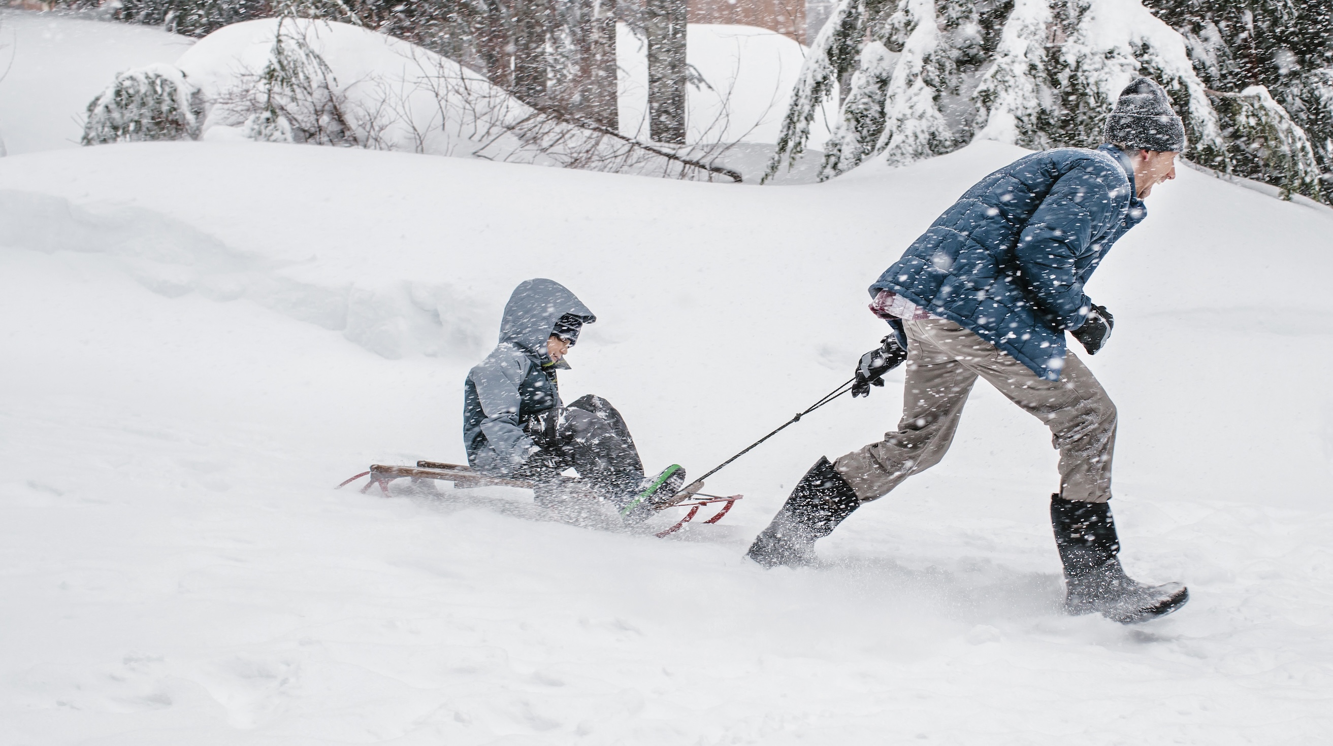 The image shown is a man running & pulling a child on a sled through a snowy winter landscape.