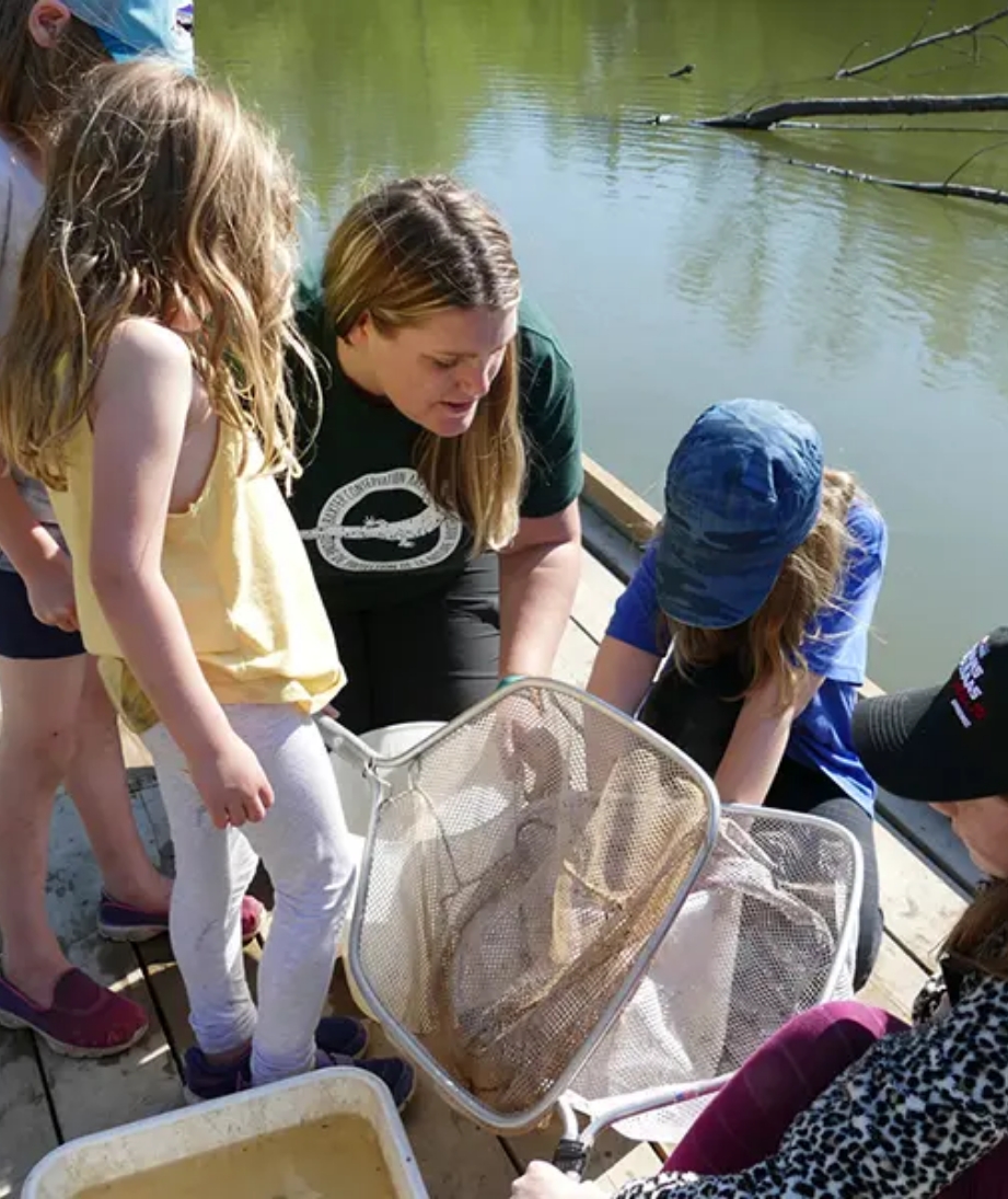 Our Featured Partners. The picture shown is a teacher and four students looking into a net to see what they caught.